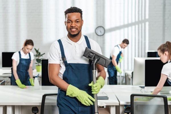Smiling,African,American,Cleaner,Holding,Vacuum,Cleaner,Brush,Near,Team